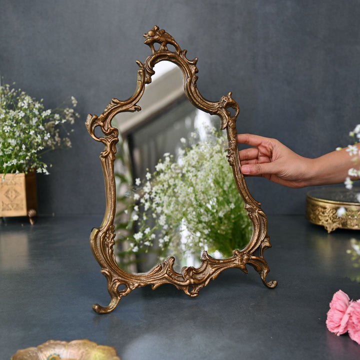 Baroque-style ornate tabletop mirror with an antique gold frame and sculpted detailing.