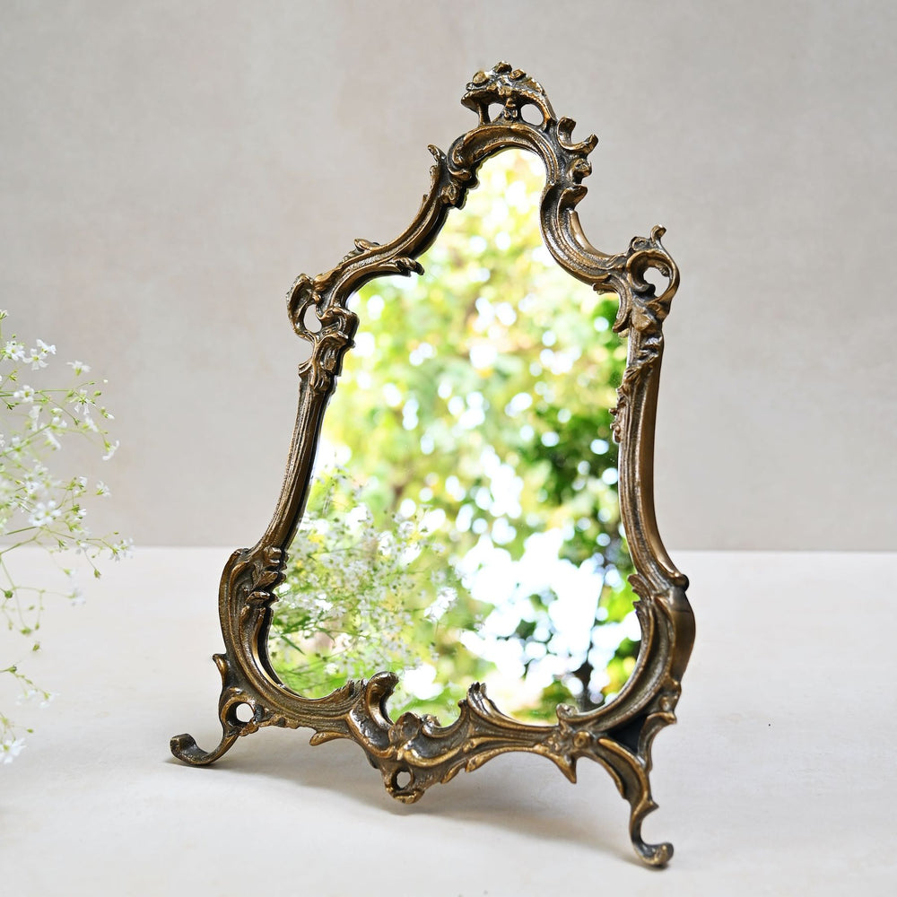 Baroque-style ornate tabletop mirror with an antique gold frame and sculpted detailing.