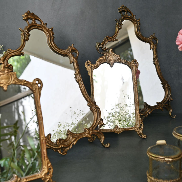 Baroque-style ornate tabletop mirror with an antique gold frame and sculpted detailing.