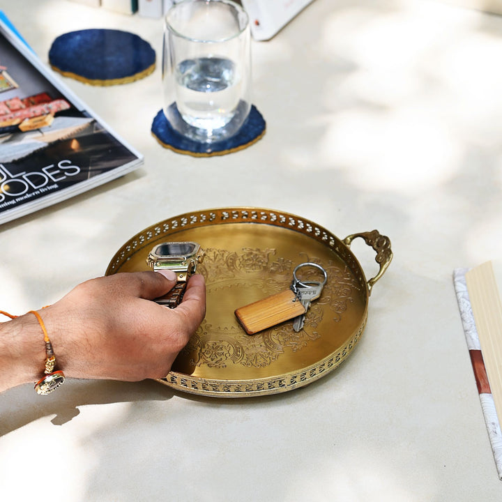 Person holding a small object over a decorative gold tray on a table.