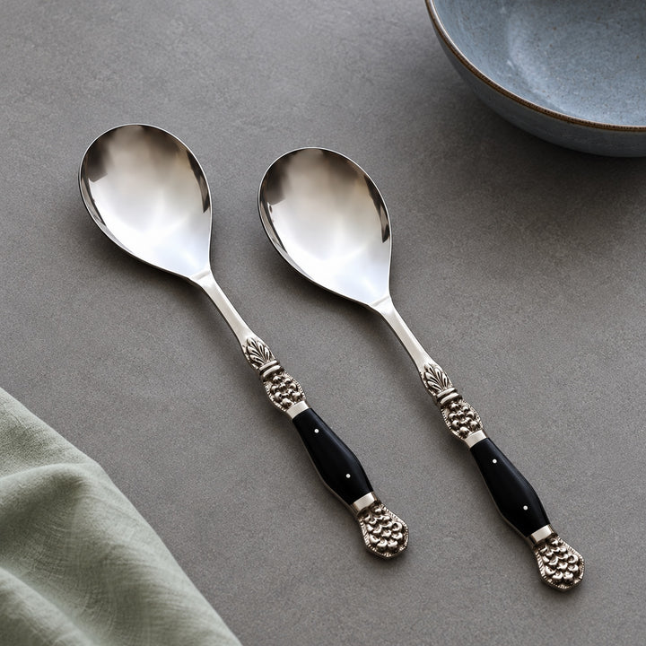 Set of two Windsor serving spoons with black resin-inlaid handles beside a green napkin and blue plate.