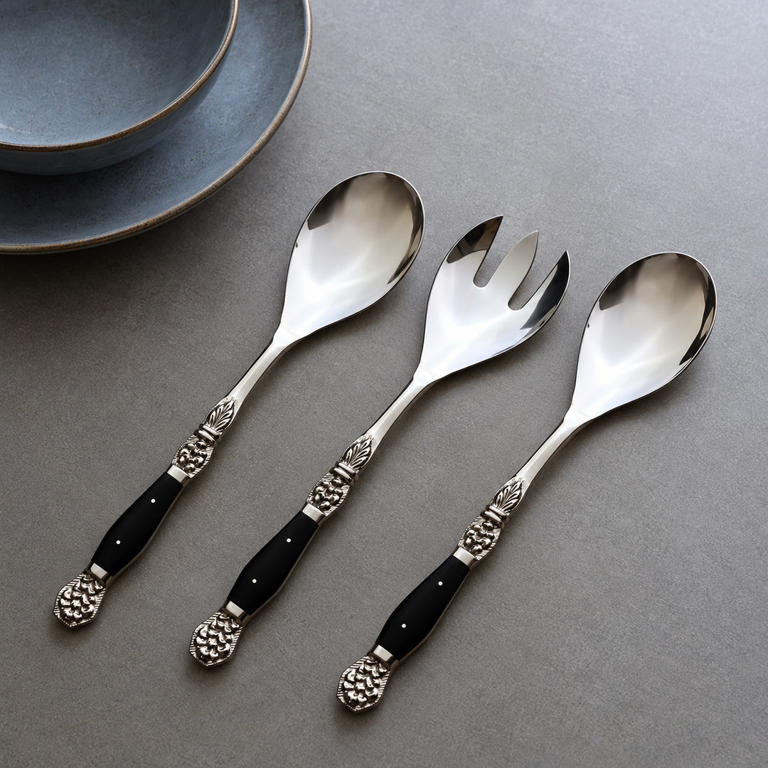 Windsor serving cutlery set of three: two spoons and one fork arranged diagonally on a grey table beside blue plates.