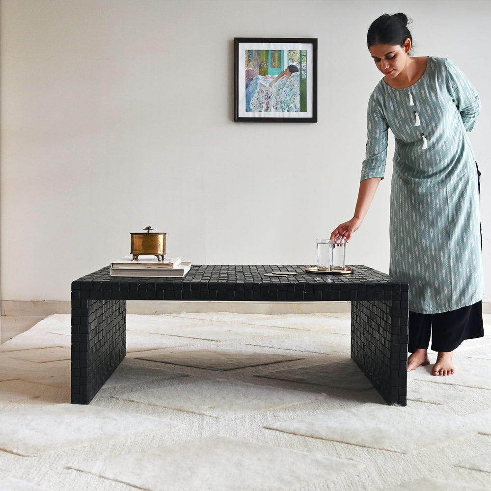 Woman arranging items on a black textured coffee table in a room with a framed picture on the wall.