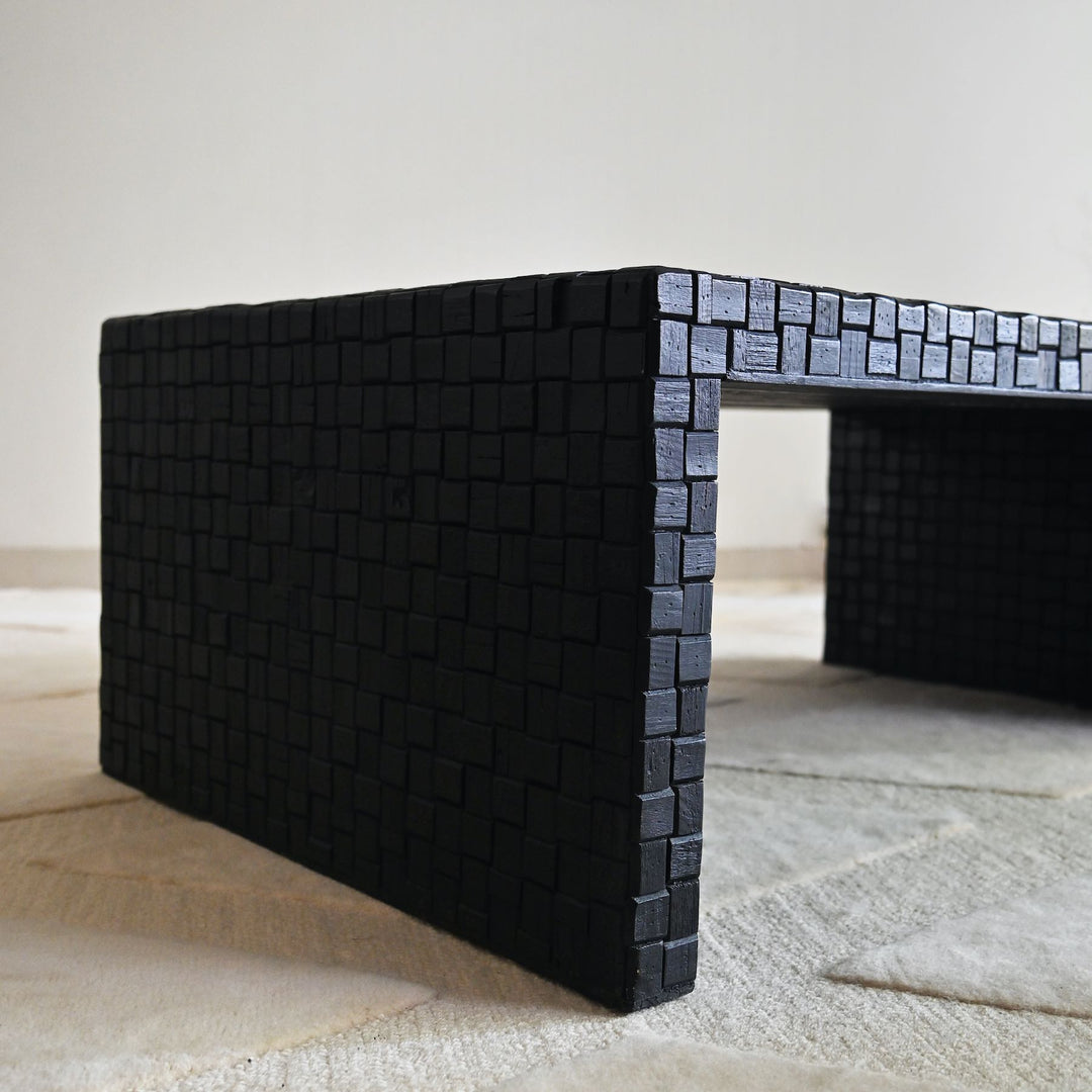 Black woven coffee table on a light wooden floor with a neutral background