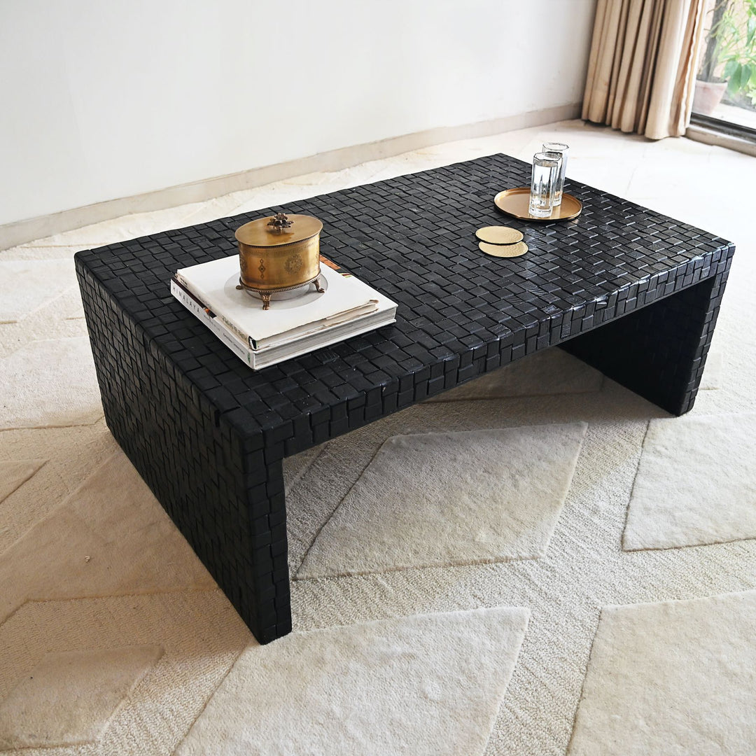 Black woven coffee table with decorative items on a stone floor