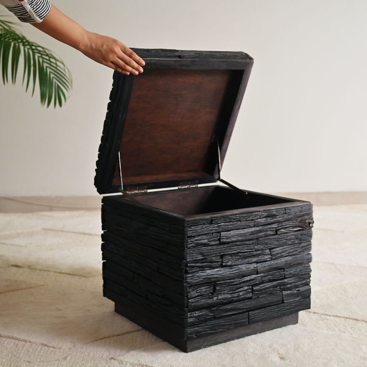 Wooden storage box with a hand opening the lid on a light wooden floor.