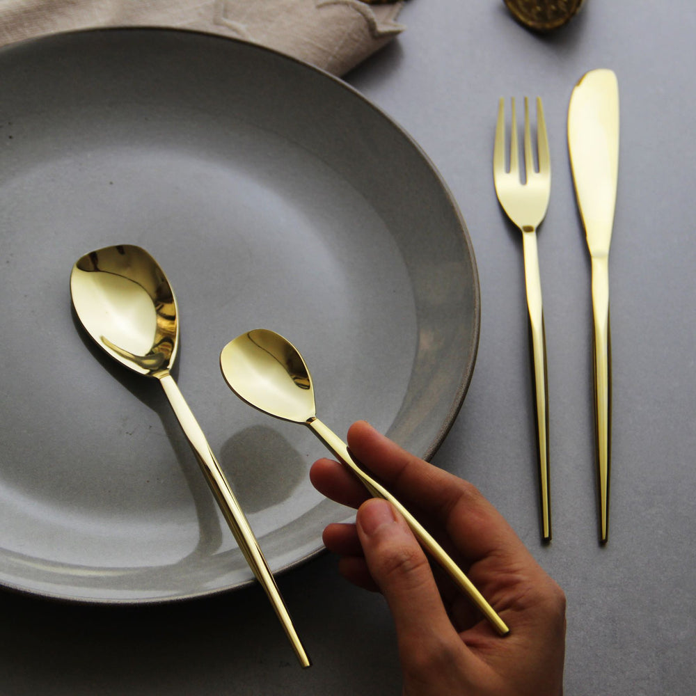 A hand holding the Aurum dessert spoon beside the table spoon, fork and knife.