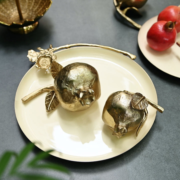 Gold decorative pomegranates on a white plate with a gray background