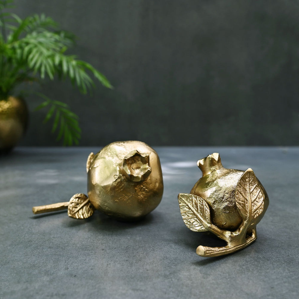 Gold pomegranate-shaped showpieces on a dark surface with a plant in the background