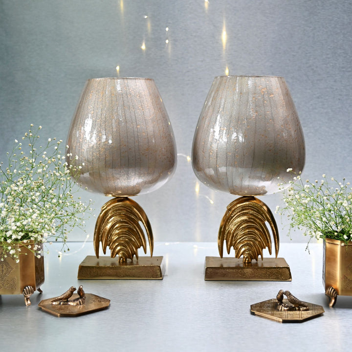 Two decorative lamps with gold bases on a reflective surface with a gray background