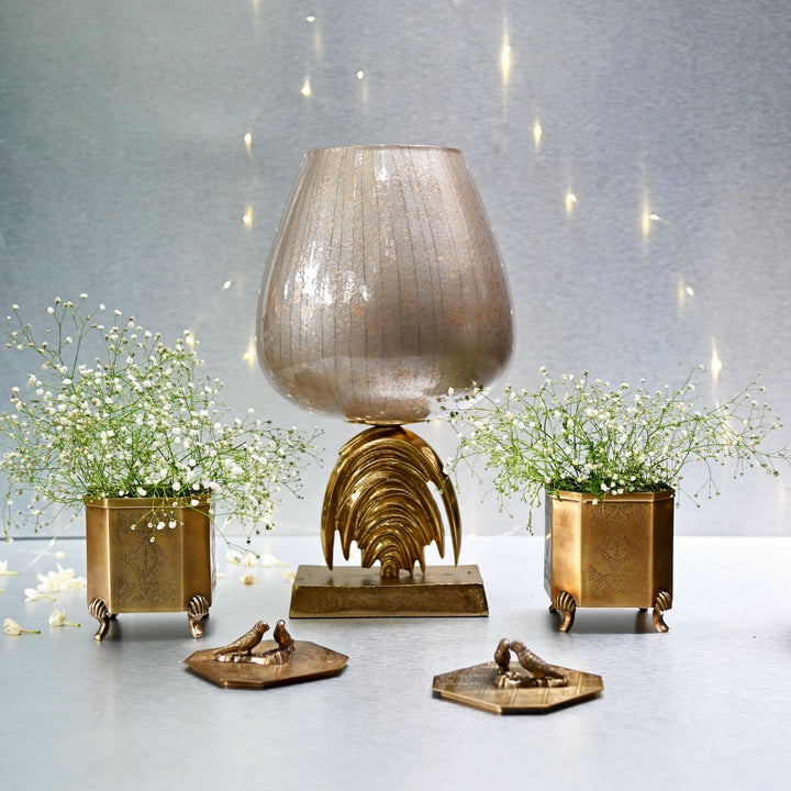 Decorative lamp with gold base and two small plants on a light gray surface.