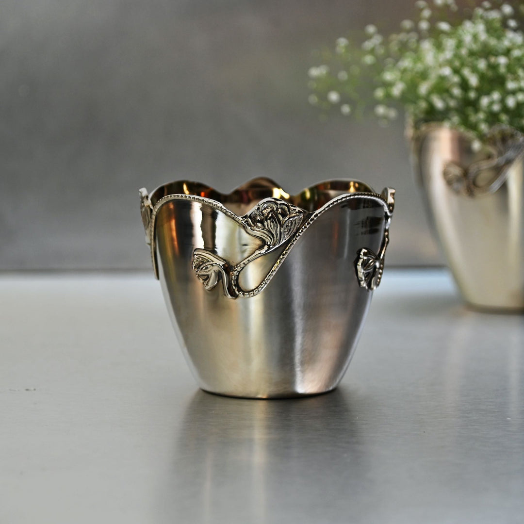 Decorative silver brass planter with intricate designs on a reflective surface.