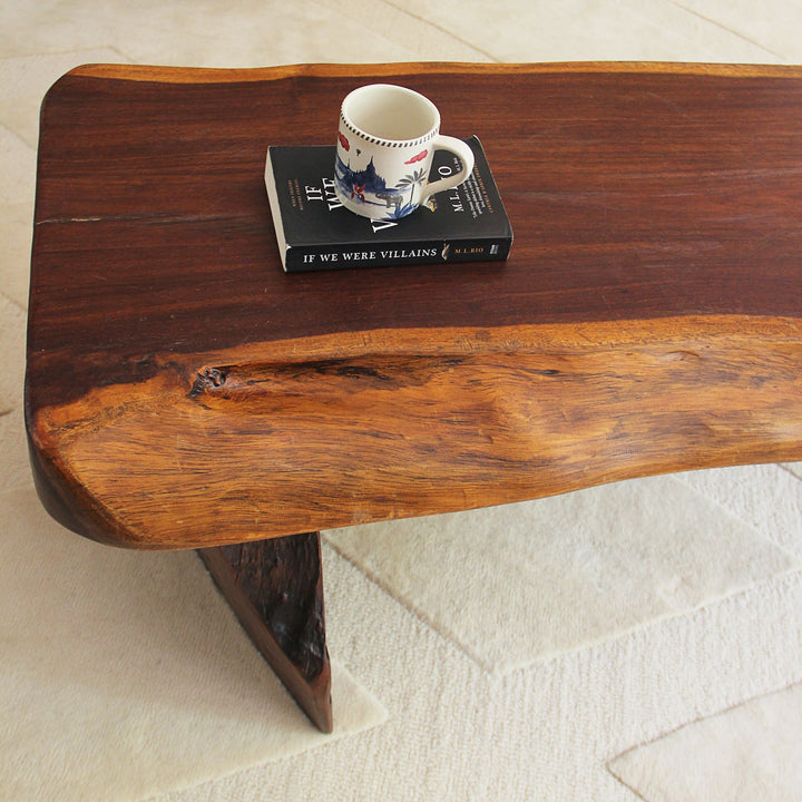 Teak wood bench with books and a cup on a light-colored floor.