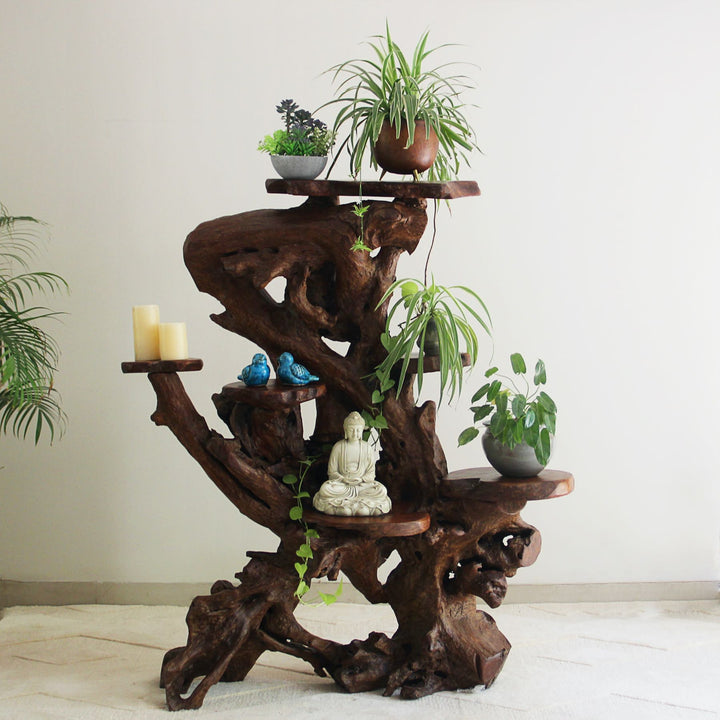 Wooden tiered shelf with plants and decorative items against a white wall.