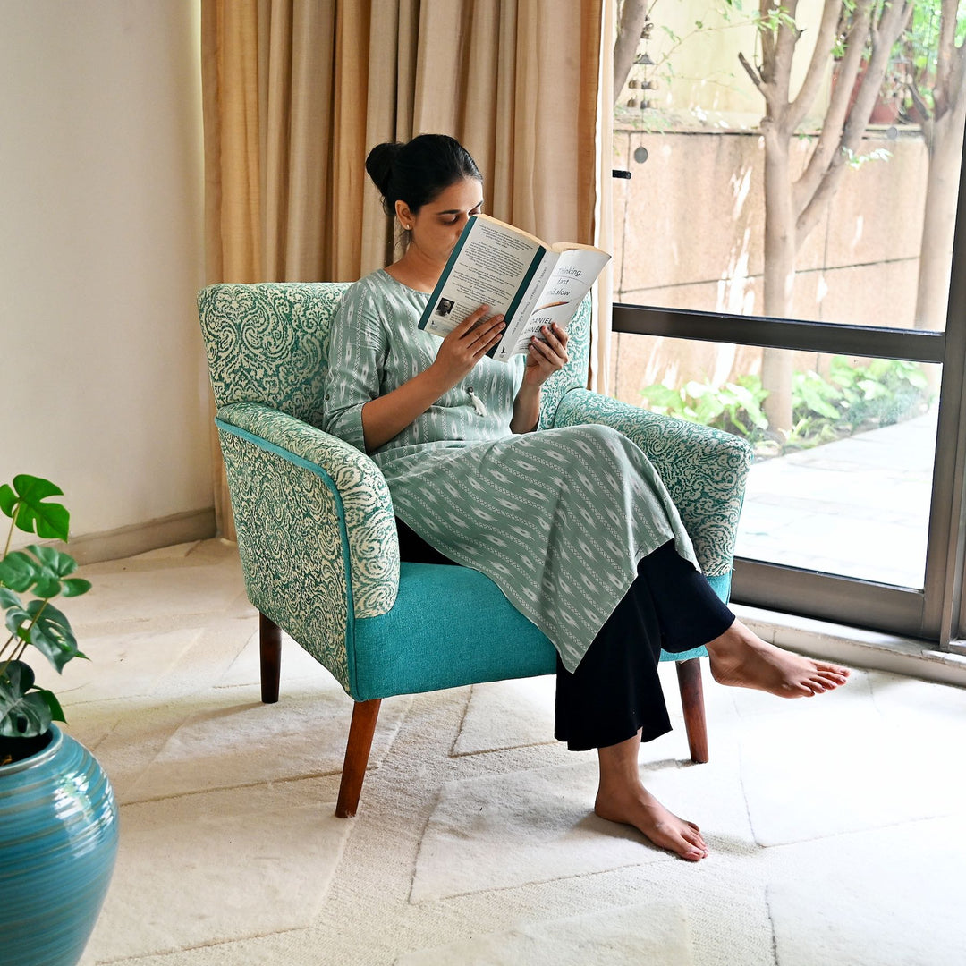 Woman reading a book in a teal armchair by a window