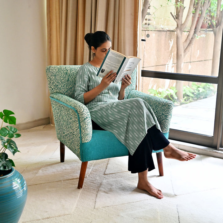 Woman reading a book in a teal armchair by a window