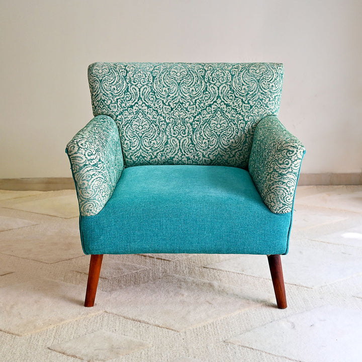 Teal armchair with patterned backrest on a light wooden floor.