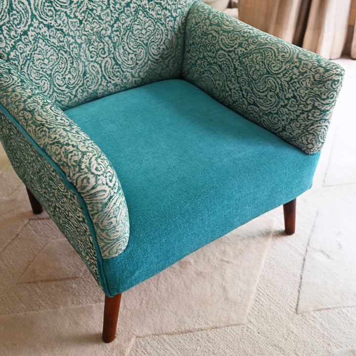 Teal armchair with patterned backrest on a light tiled floor