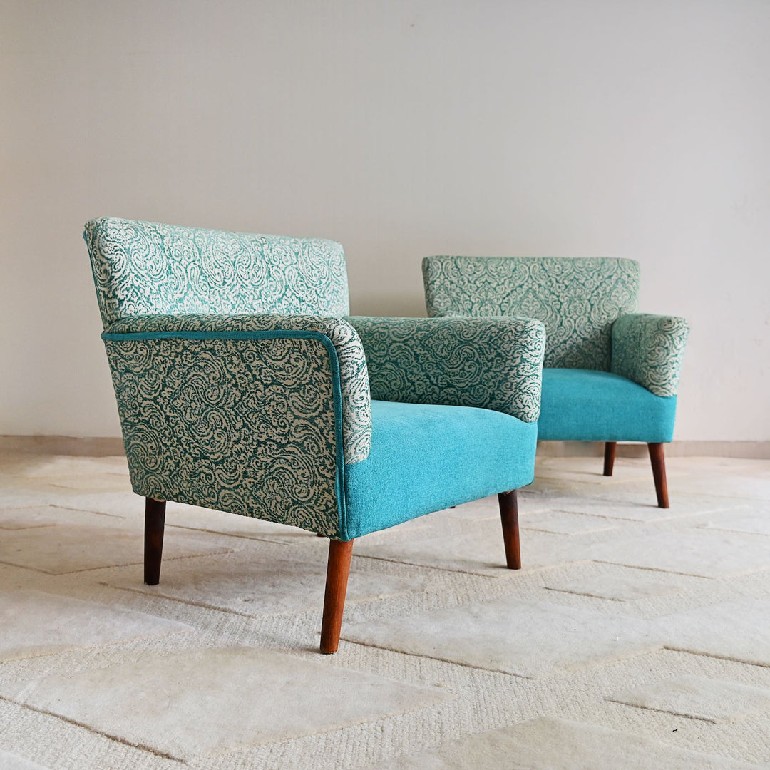 Two patterned armchairs with turquoise and green fabric on a wooden floor.