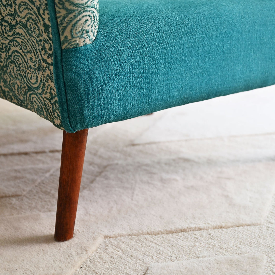 Teal upholstered chair with wooden leg on a light wood floor