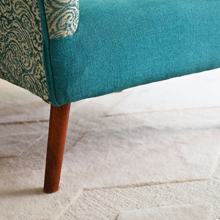 Teal upholstered chair with wooden leg on a light wood floor