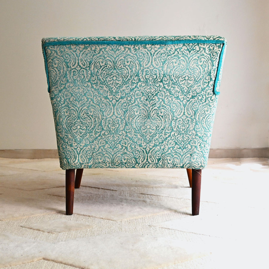 Teal patterned chair with wooden legs on a light wooden floor.