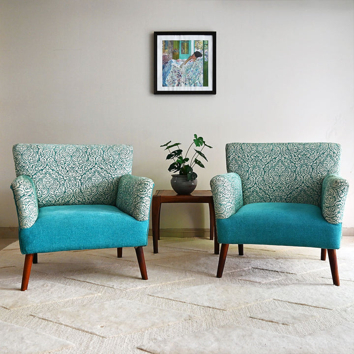 Two teal armchairs with patterned backrests in a room with a framed picture on the wall.
