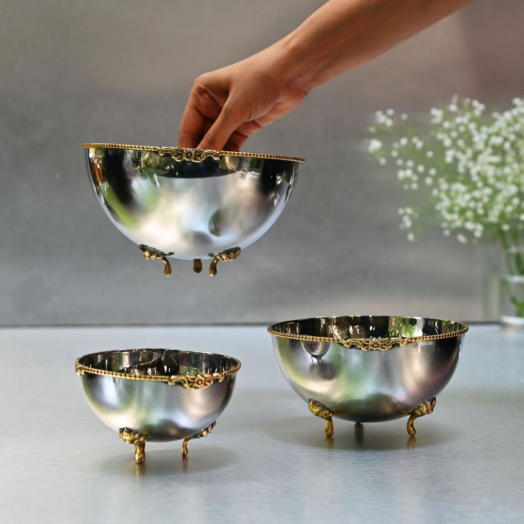 Set of three silver bowls with gold accents on a light surface.