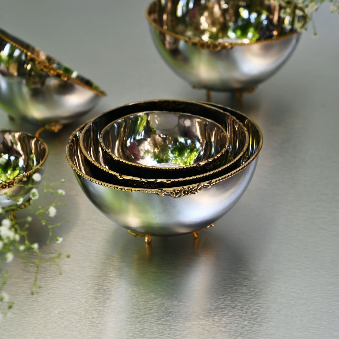 Set of silver bowls with gold rims on a reflective surface