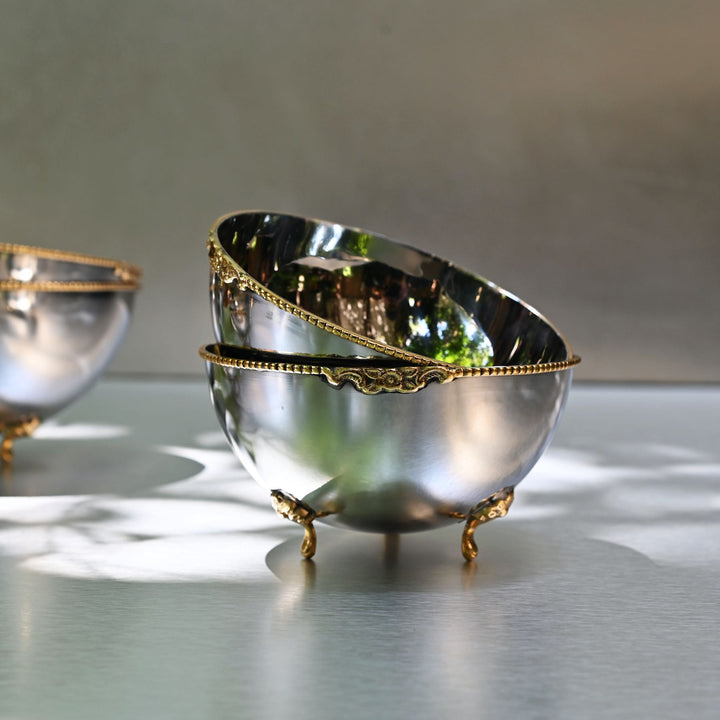 Decorative silver bowls with gold accents on a reflective surface