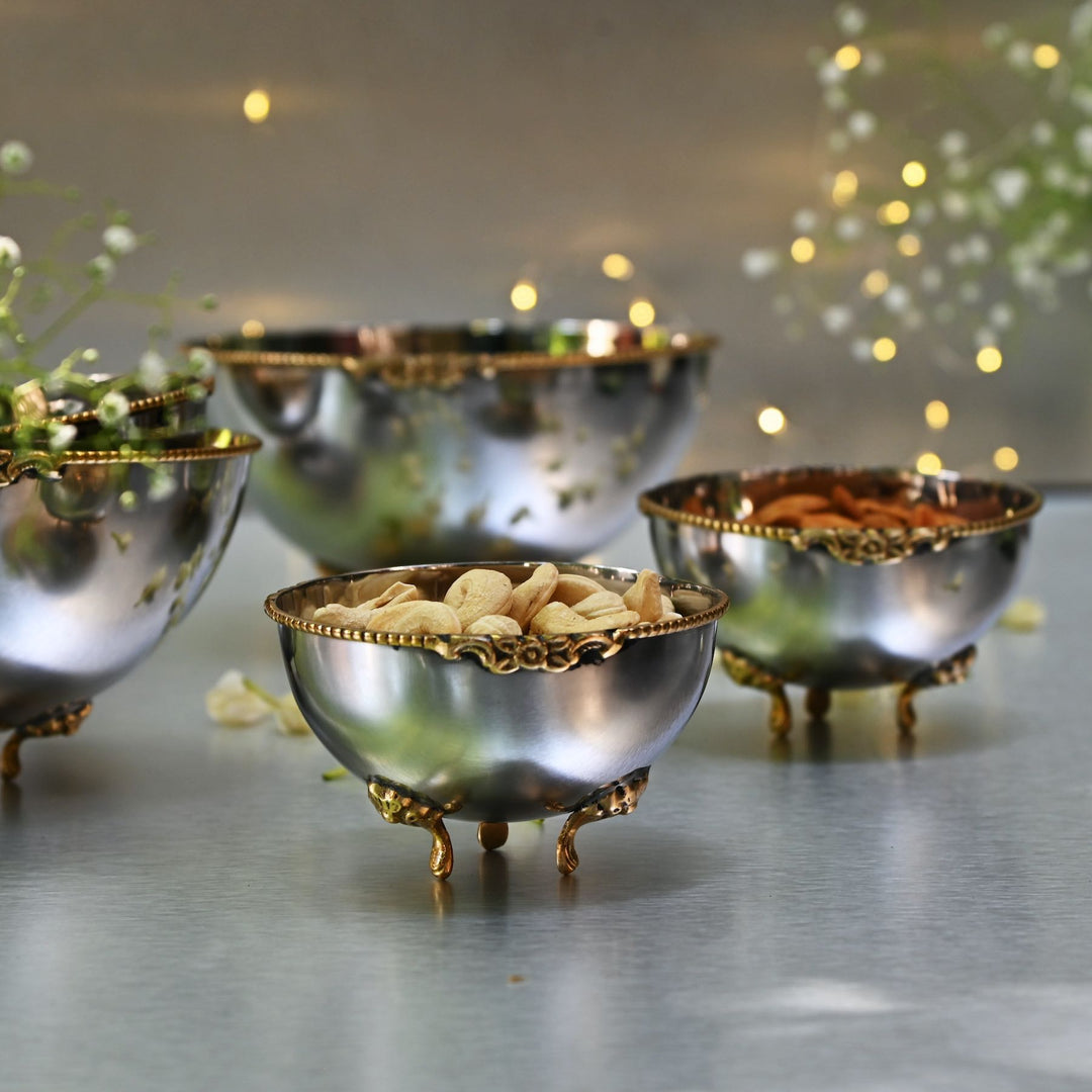 Set of decorative metal bowls with gold rims on a reflective surface.