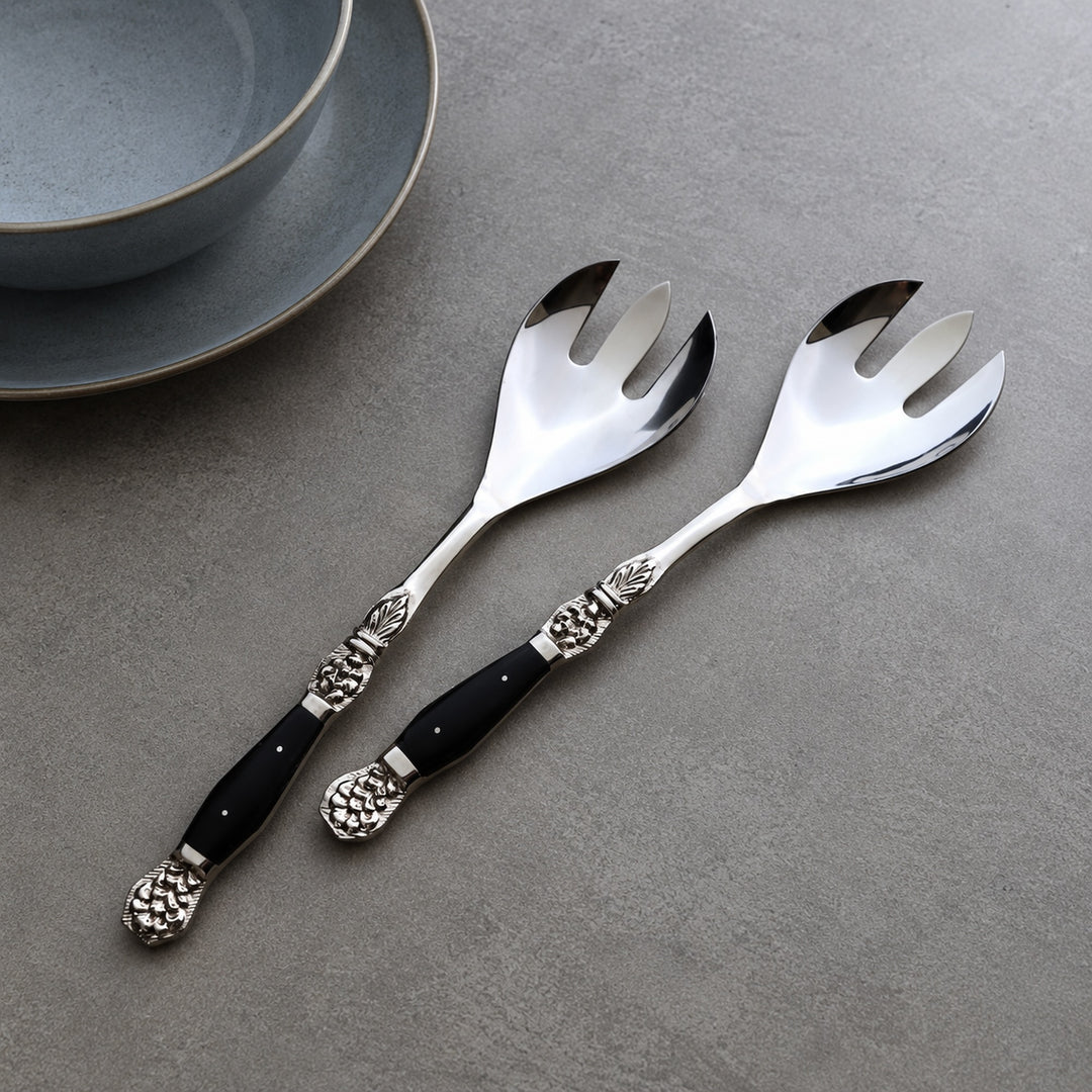 Set of two Windsor serving forks with black resin-inlaid handles beside blue plates.