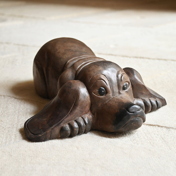 Front view of the wooden dog sculpture lying with its chin between its paws.
