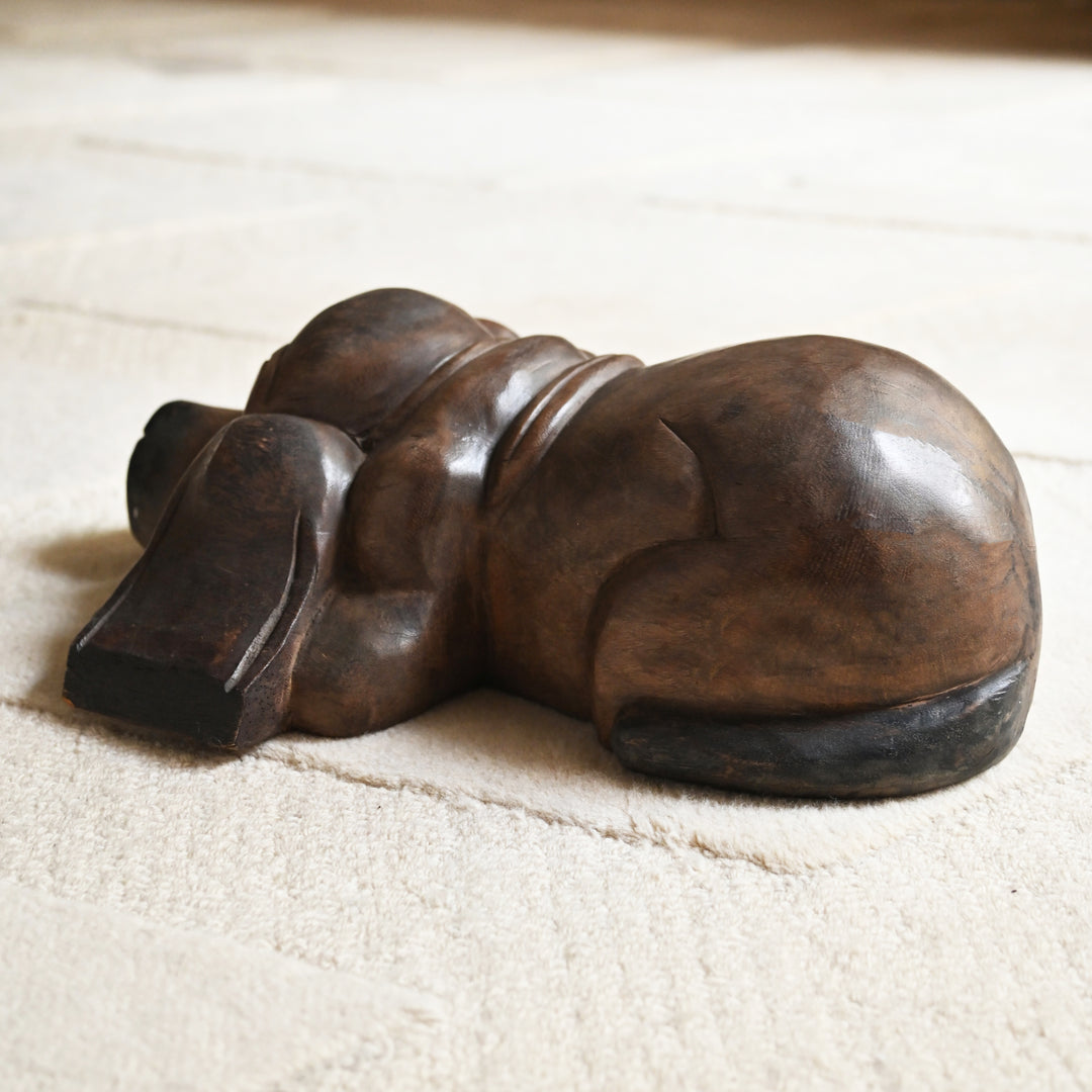 Rear view of the carved wooden dog showing its rounded back and curled tail.