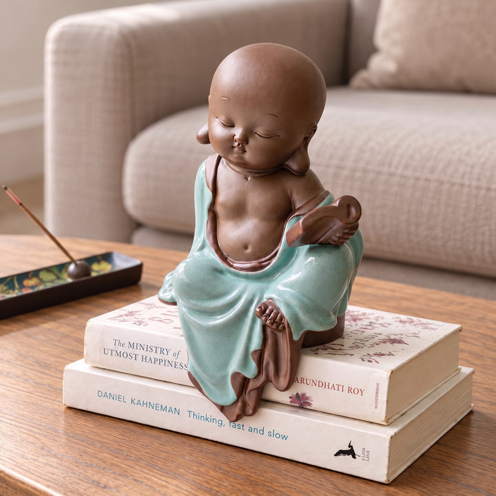 Celadon monk figurine in glazed green robes, sitting on stacked books on a coffee table.