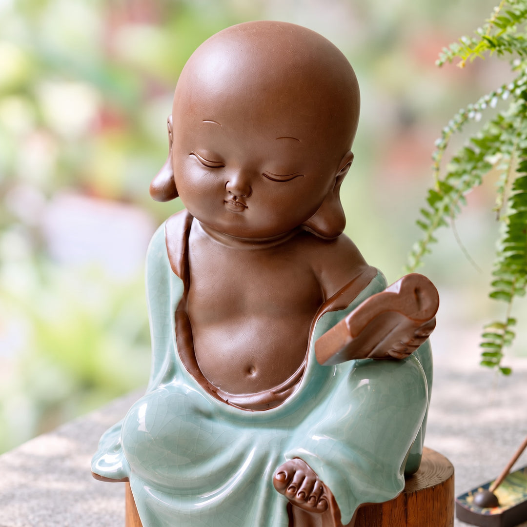 Close-up of the ceramic monk figurine's delicately modelled face, book and celadon-glazed robes.