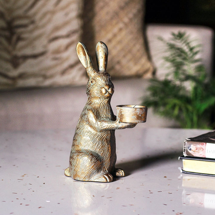 Aluminium rabbit candle holder beside books, with long upright ears and gold finish